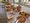 Ein reichhaltiges Frühstücksbuffet auf einem langen Tisch. Schüsseln mit Müsli und Joghurt, frisches Obst wie Melone und Trauben, Brotkörbe und Saftkartons sind zu sehen. Der Tisch steht in einem hellen Raum mit großen Fenstern, die auf eine Terrasse hinausführen.