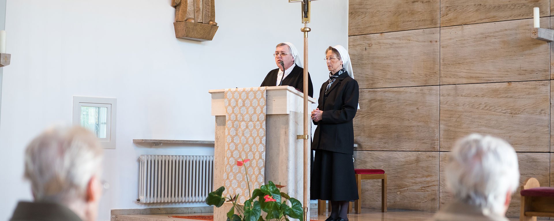 Gottesdienst: zwei Ordensschwestern am Pult - Kirchgänger im Vordergrund