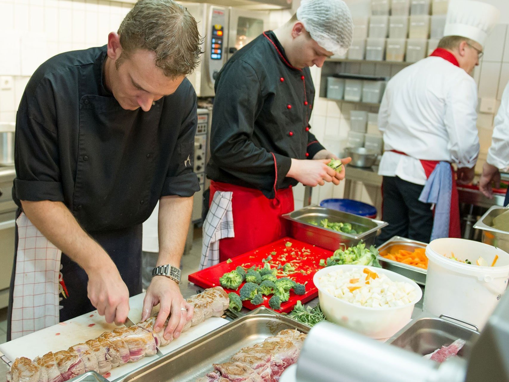 Küche: Köche schneiden Gemüse und Fleisch