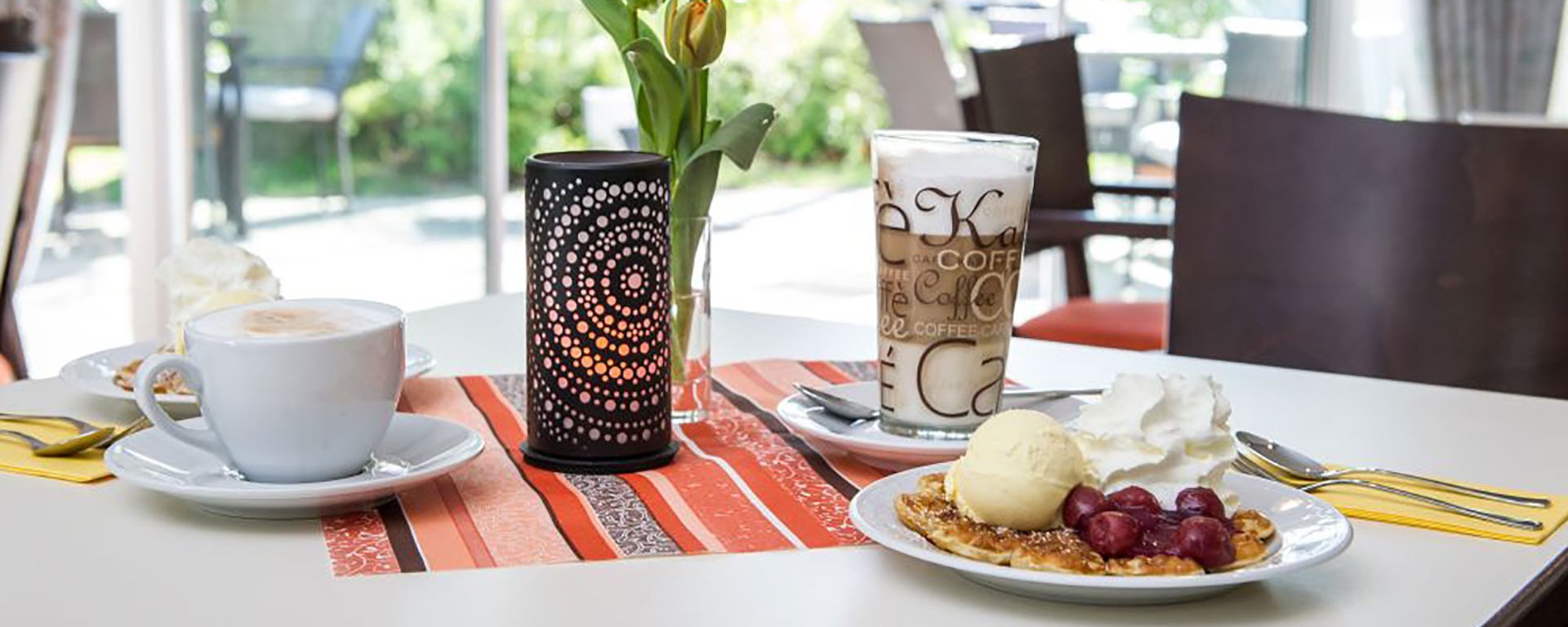 Nahaufnahme: Nachspeise auf einem kleinen Tisch - Waffeln mit Kirschen und Sahne - dazu Kaffee