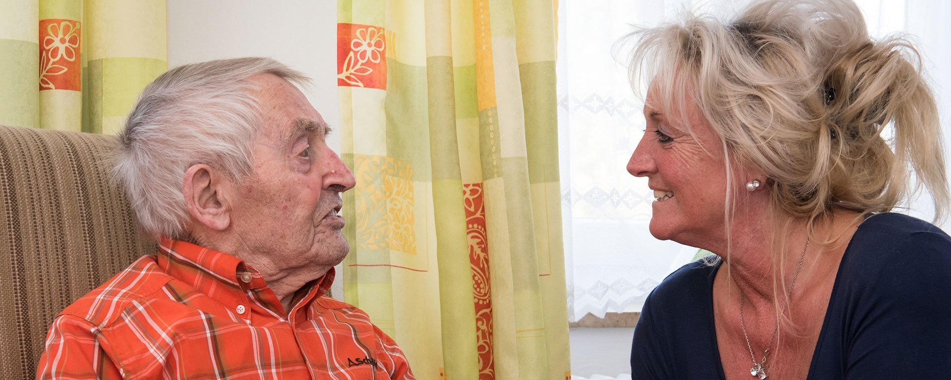 Ein Bewohner sitzt im Sessel und erklärt einer ihm gegenübersitzenden Pflegerin etwas