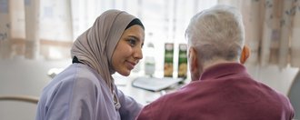 Eine junge Pflegerin mit Kopftuch füttert einen älteren Herrn.