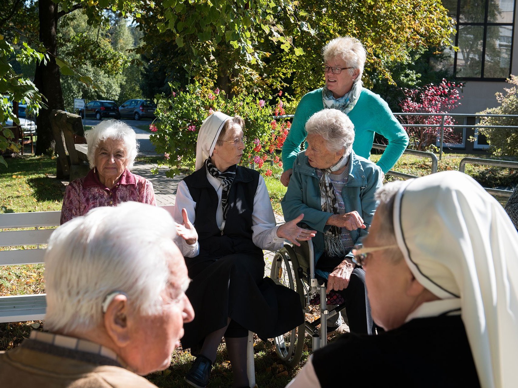 Eine Gruppe Senioren unterhält sich auf Parkbänken mit zwei Ordensschwestern