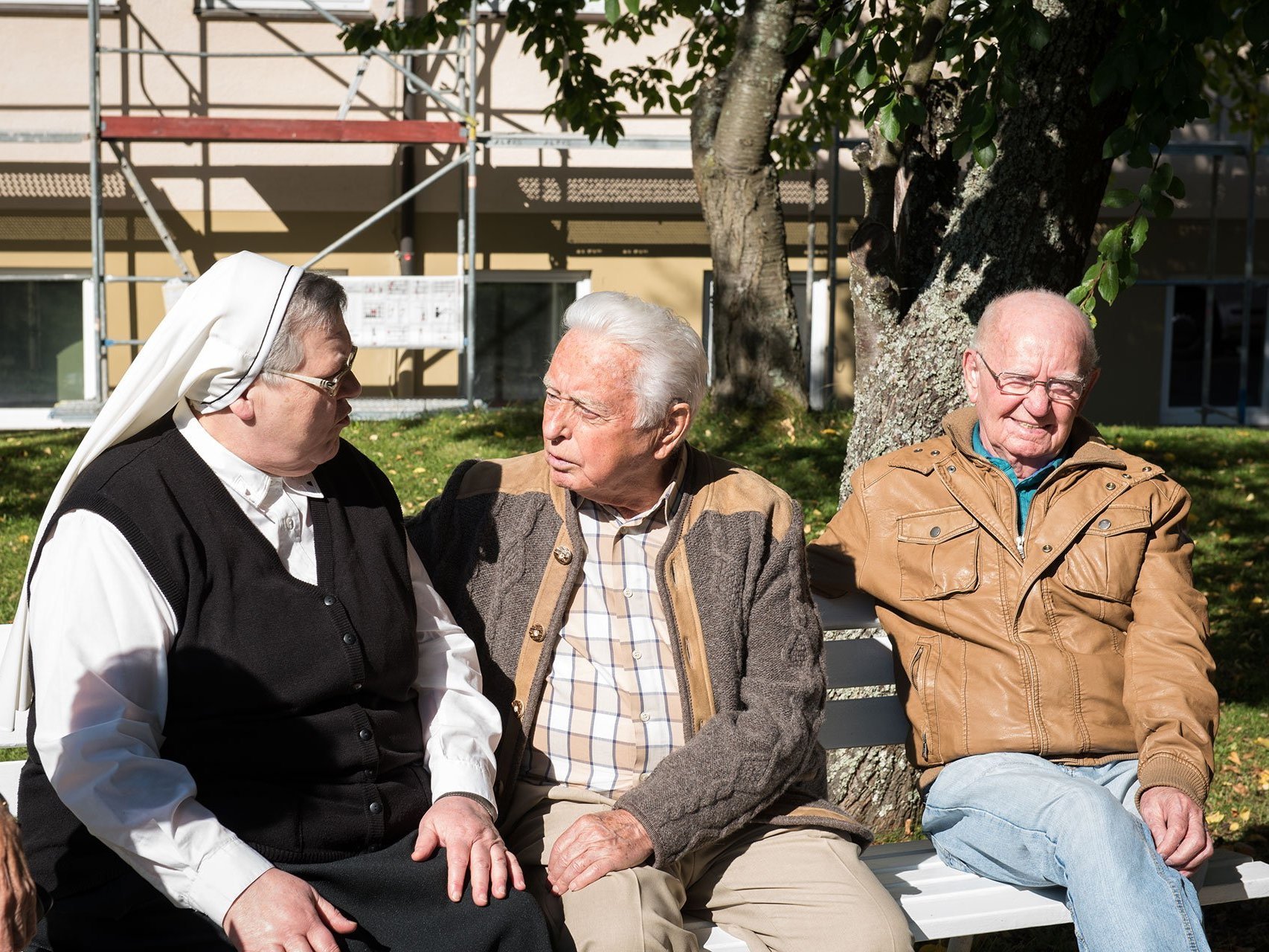 Zwei Männer sitzen auf einer Parkbank - einer unterhält sich mit einer Ordensschwester